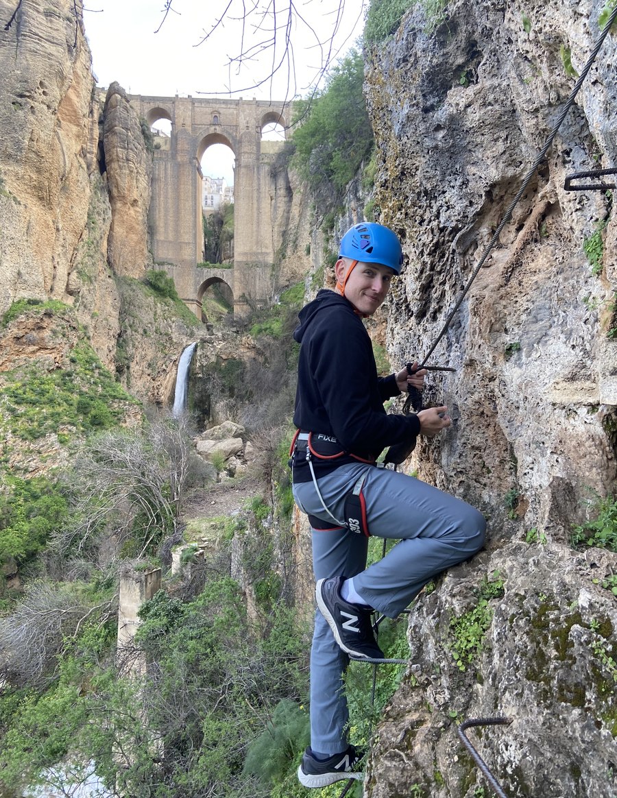 Cody A. Ray on a via ferrata above Ronda, Spain, with the Puente Nuevo bridge in the background